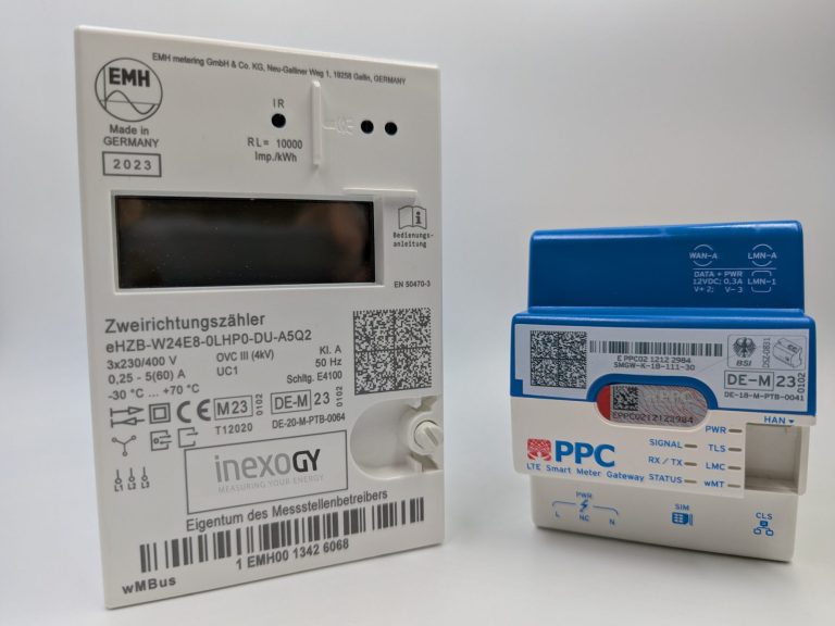 Smart Meter Zwei Stromzähler auf einem Tisch, einer mit grauer Rückseite und der andere blau.